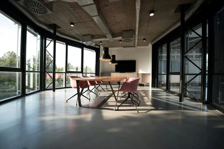 An empty conference room with a long wooden table and pink chairs