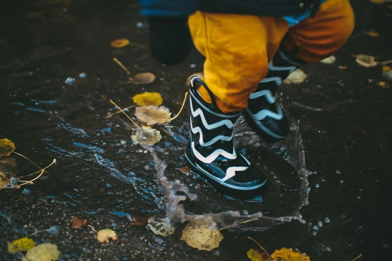 A child in striped rain boots splashing through a puddle
