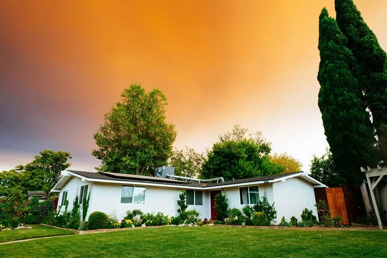 A single-story white house under an orange evening sky